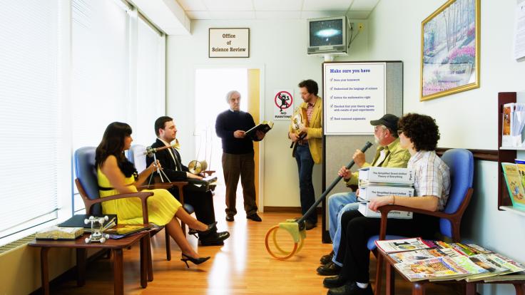 "Outsider" scientists await approval for their creations in a pretend office setting