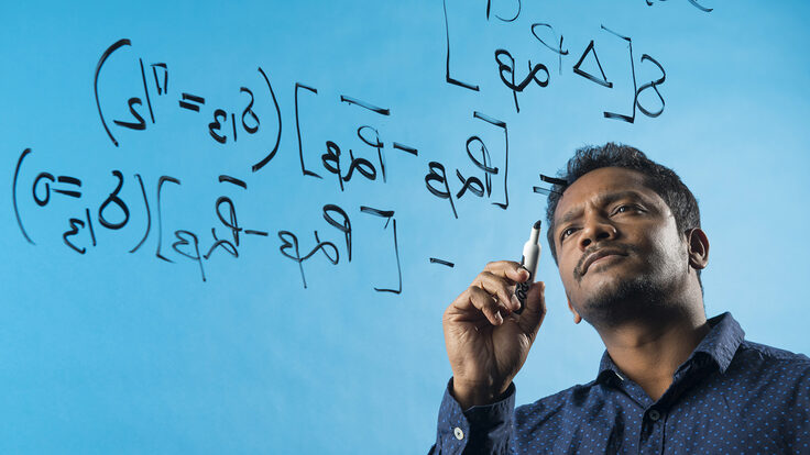 Jogesh Rout writing equations on a clear panel. The background is blue.