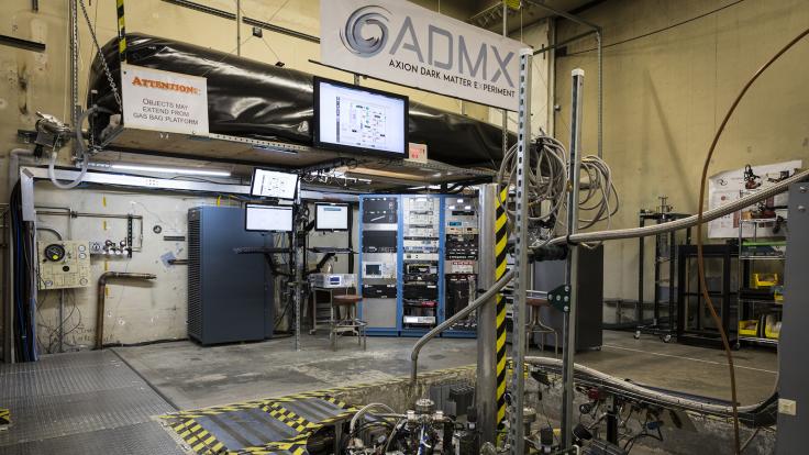 Equipment and panels for the ADMX experiment fill the room. An ADMX experiment banner hangs above.