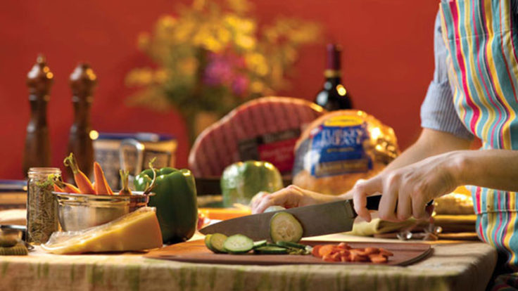 Photo of woman cooking in kitchen, cutting vegetables at board