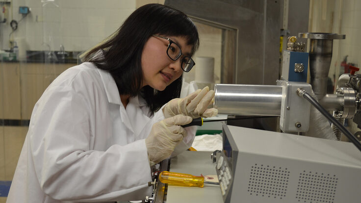 Wenzhao Wei, dressed in a white coat and gloves, works in a lab.